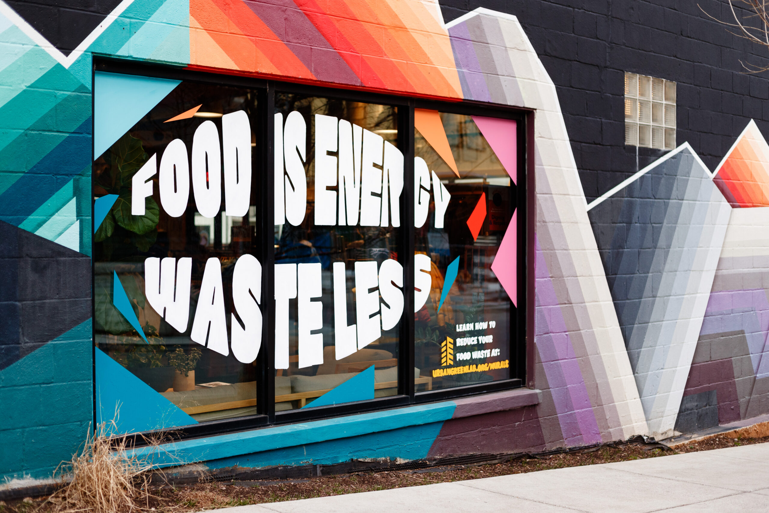 Mural that says "Food is energy. Waste less." painted on a store window