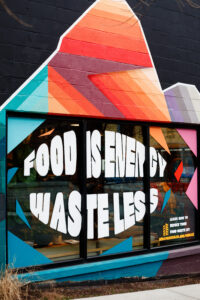 Mural that says "Food is energy. Waste less." painted on a store window