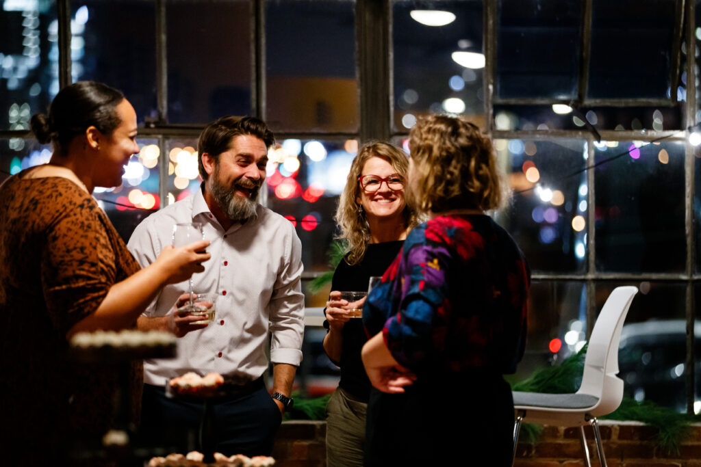 Four people laughing and talking with drinks in their hand