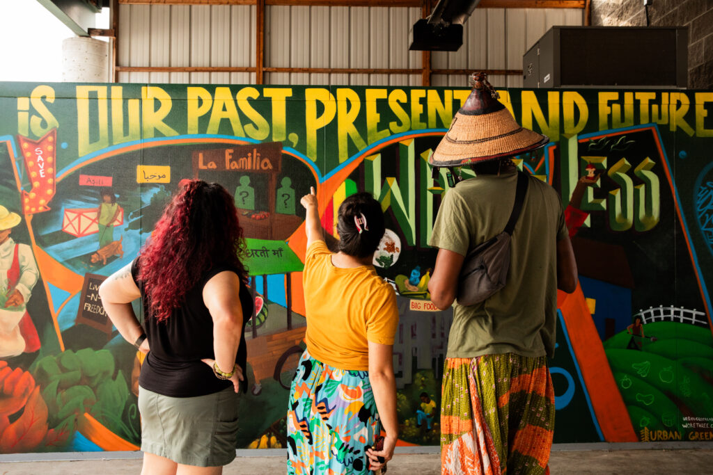 three people with their backs facing the camera pointing at a large mural that says food is our past, present, and future