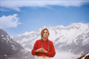woman in red sweater standing with snow-capped mountains in the background