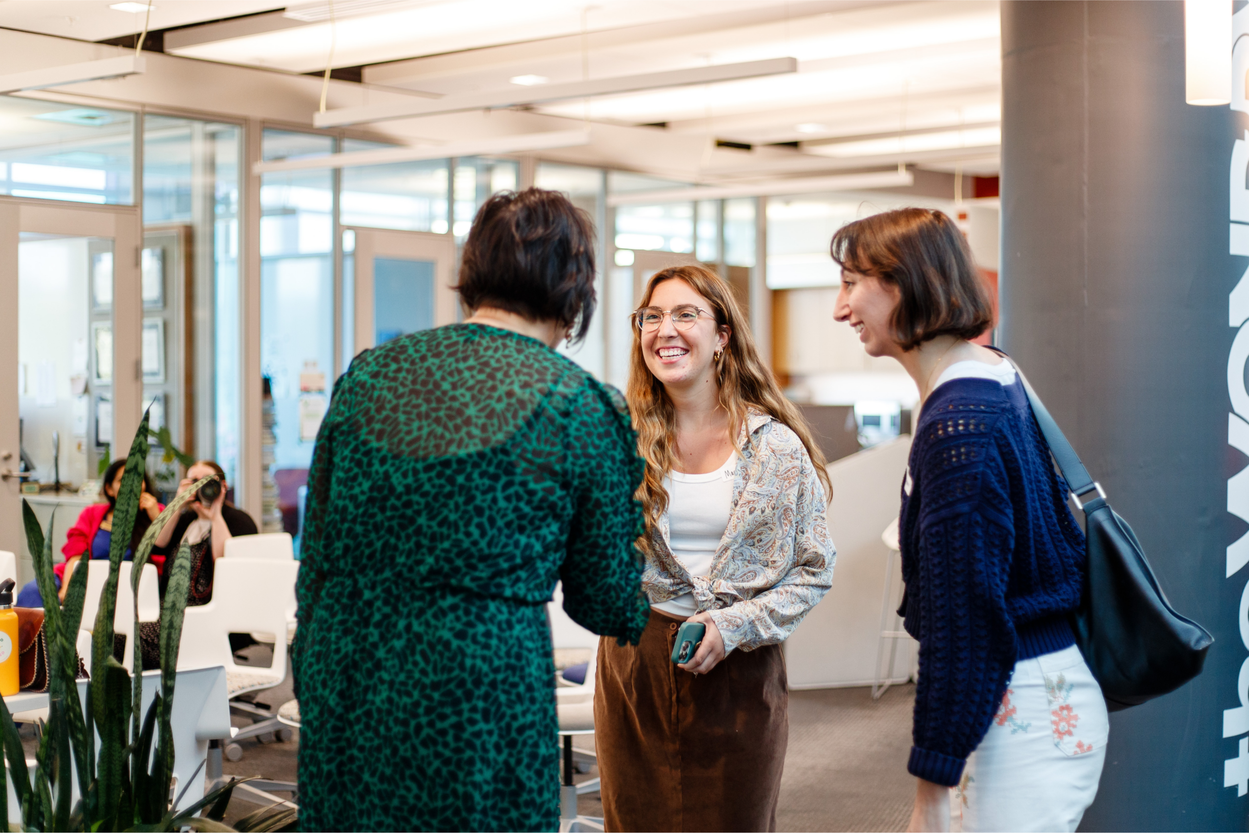 group of three women greeting each other in a brightly lit office
