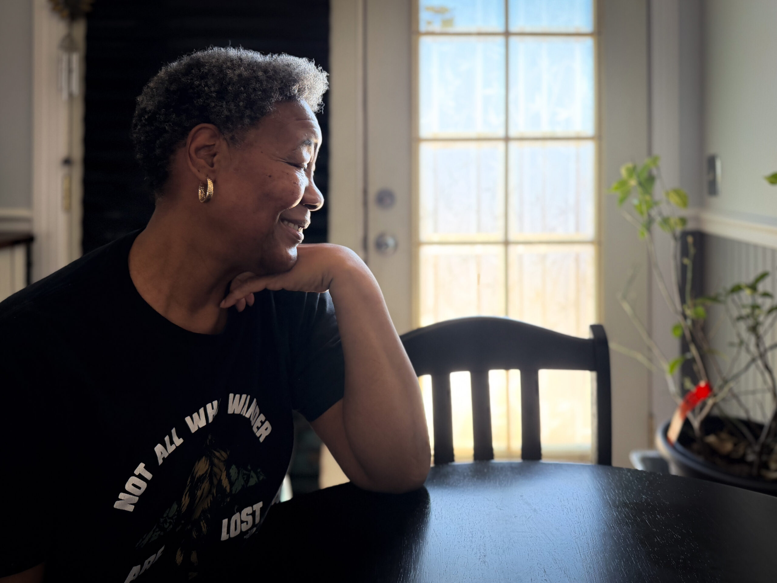 woman with her wrist under her chin looks to the right over her kitchen table and out the window