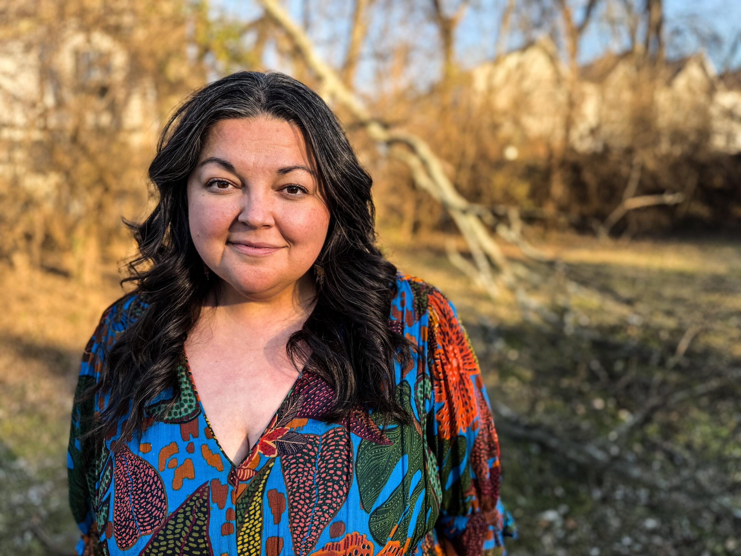 darkk-haired woman in a colorful top with winter-bare trees in the background