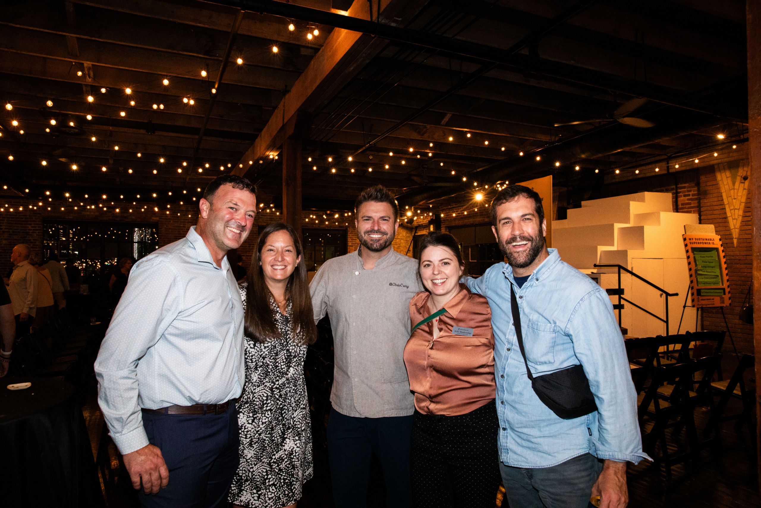 group of people smiling with a chef at an evening event under twinkle lights