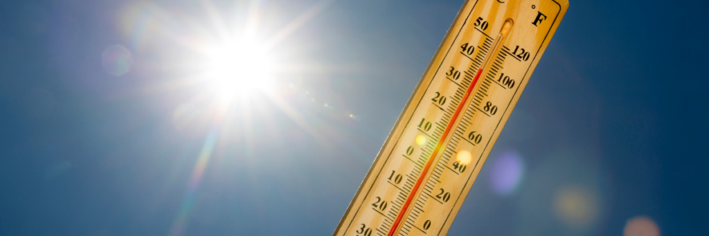 sun shines behind an analog thermometer showing 100 degrees Farenheit.