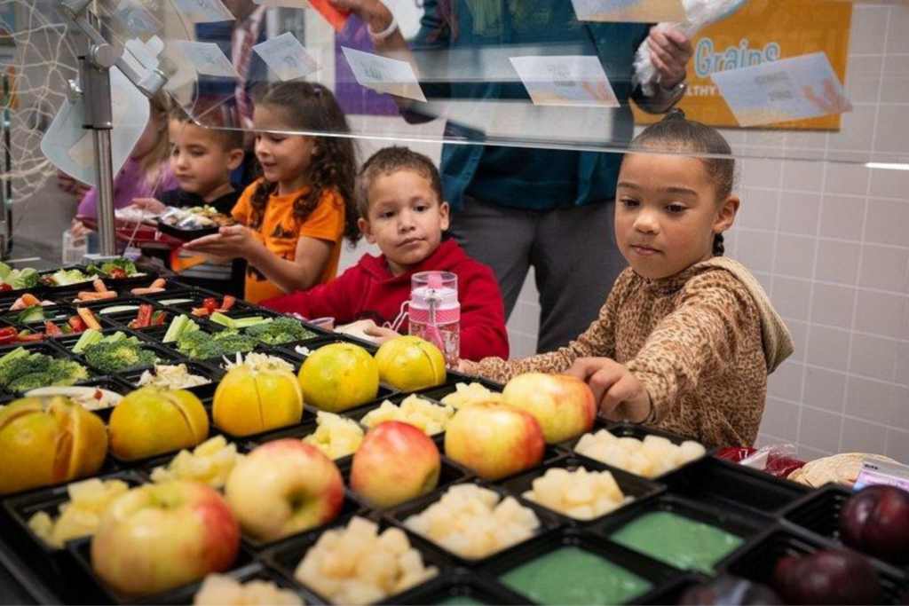 child looking at fresh apples on a table in a school lunch line