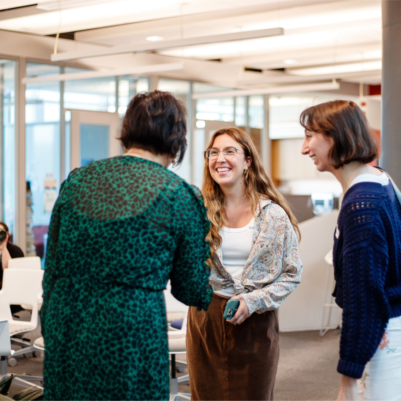 group of three women greeting each other in a brightly lit office