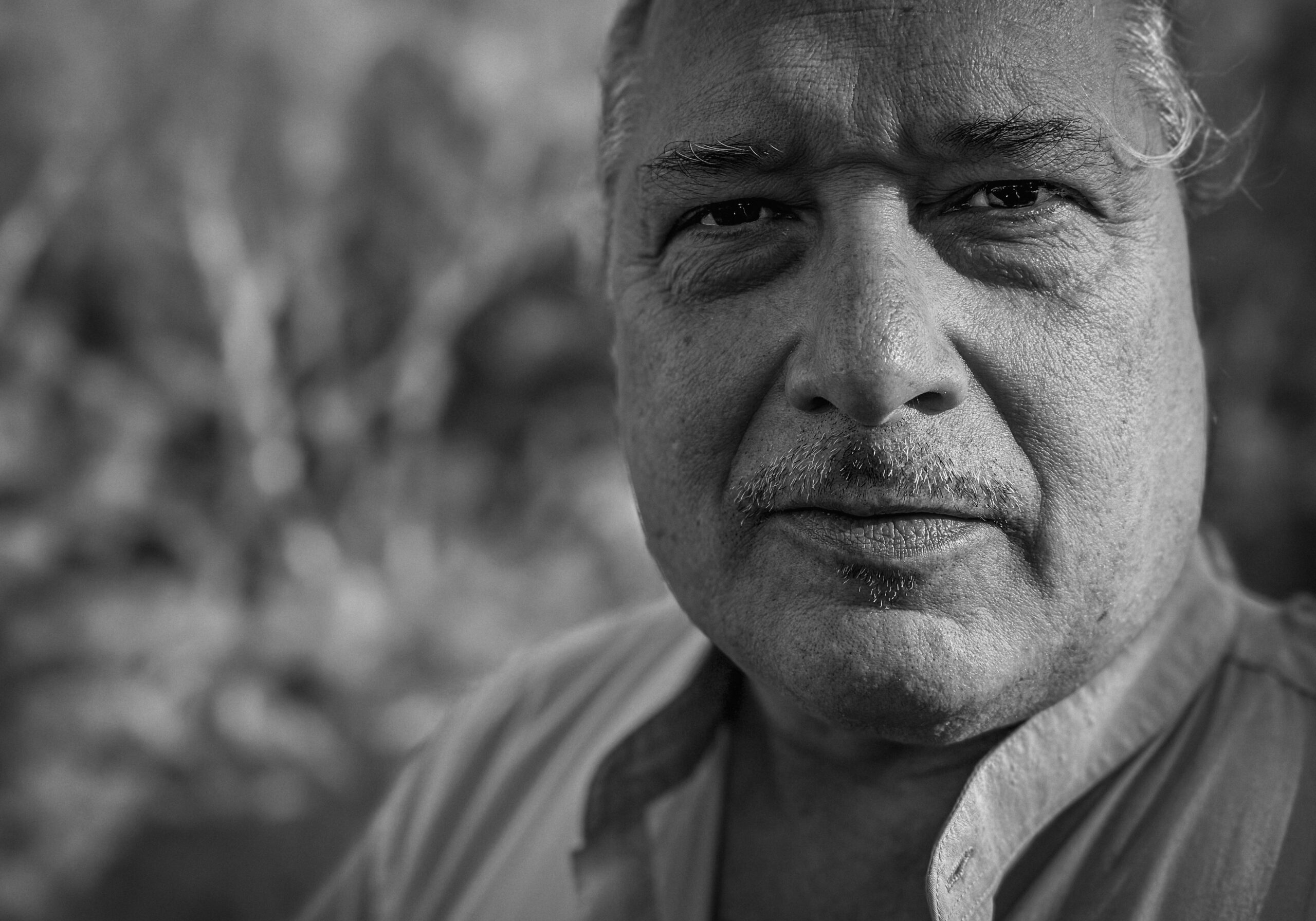 Kunesh_Tom_032625 Close black and white headshot of man with mustache in a collared shirt