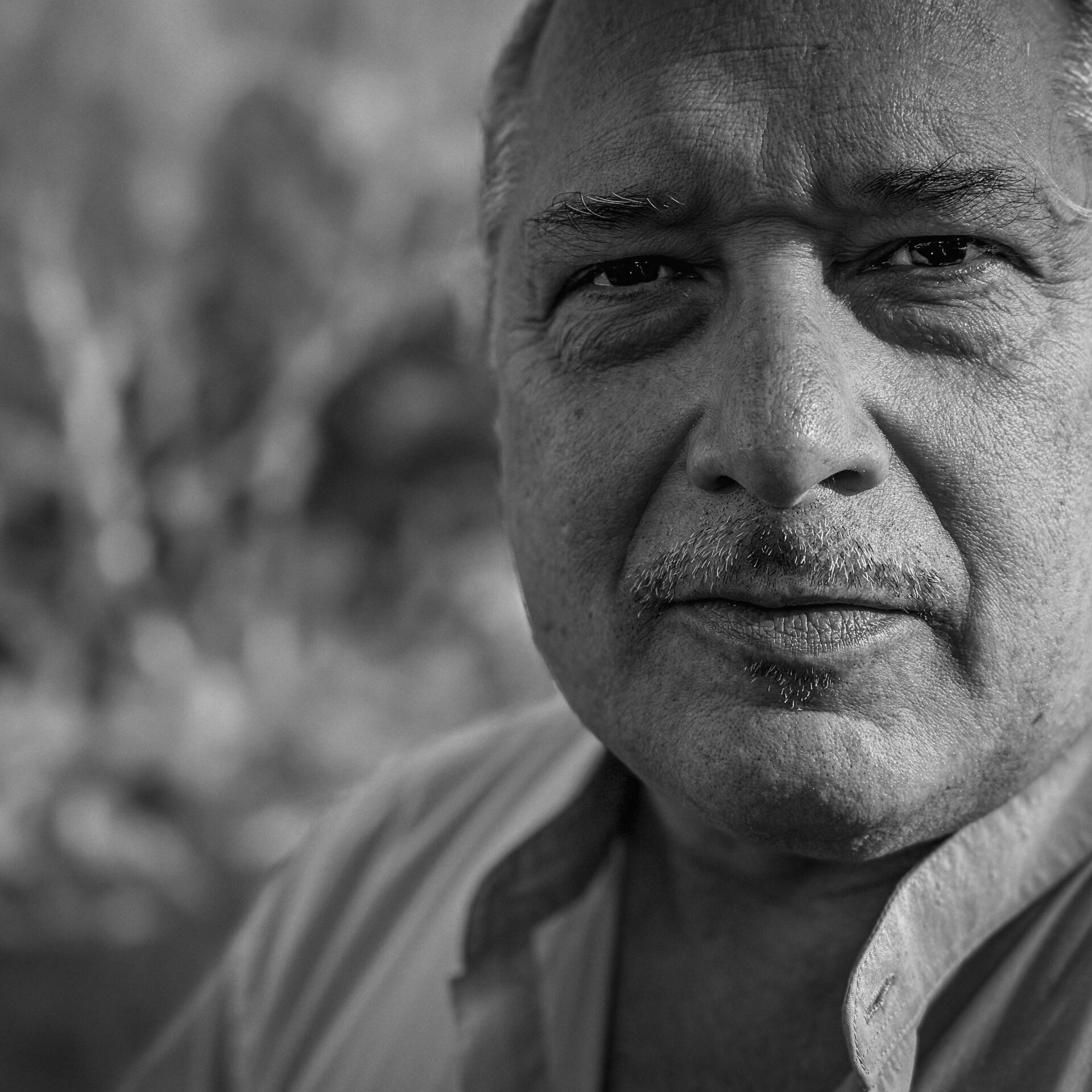 Close black and white headshot of man with mustache in a collared shirt