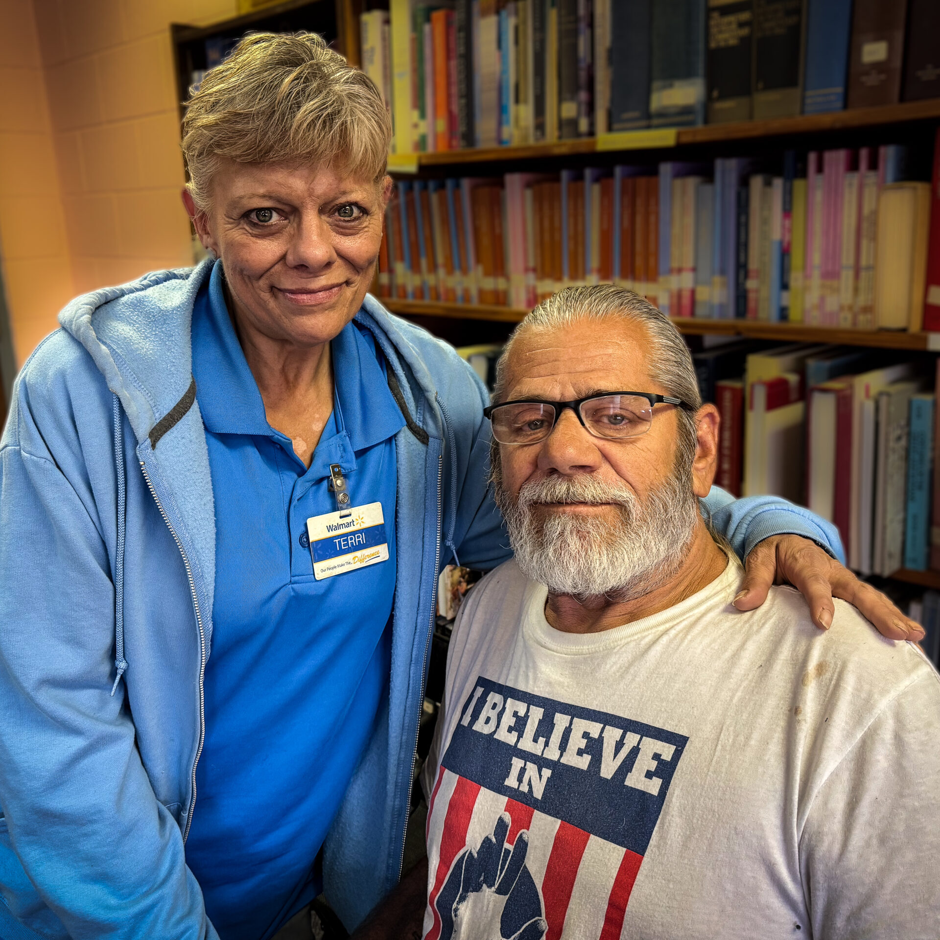 man and woman in a side embrace in front of a bookshelf
