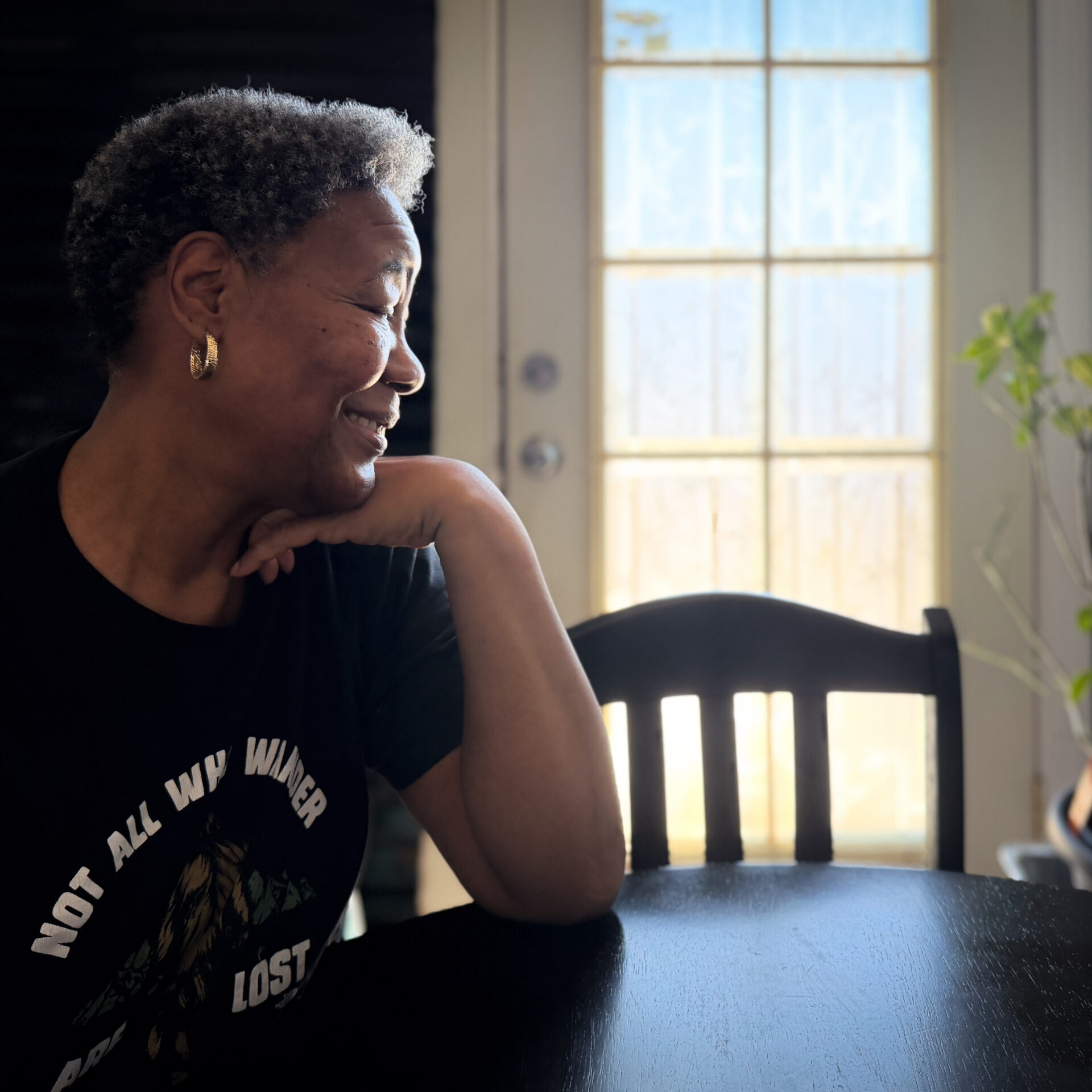 woman with her wrist under her chin looks to the right over her kitchen table and out the window