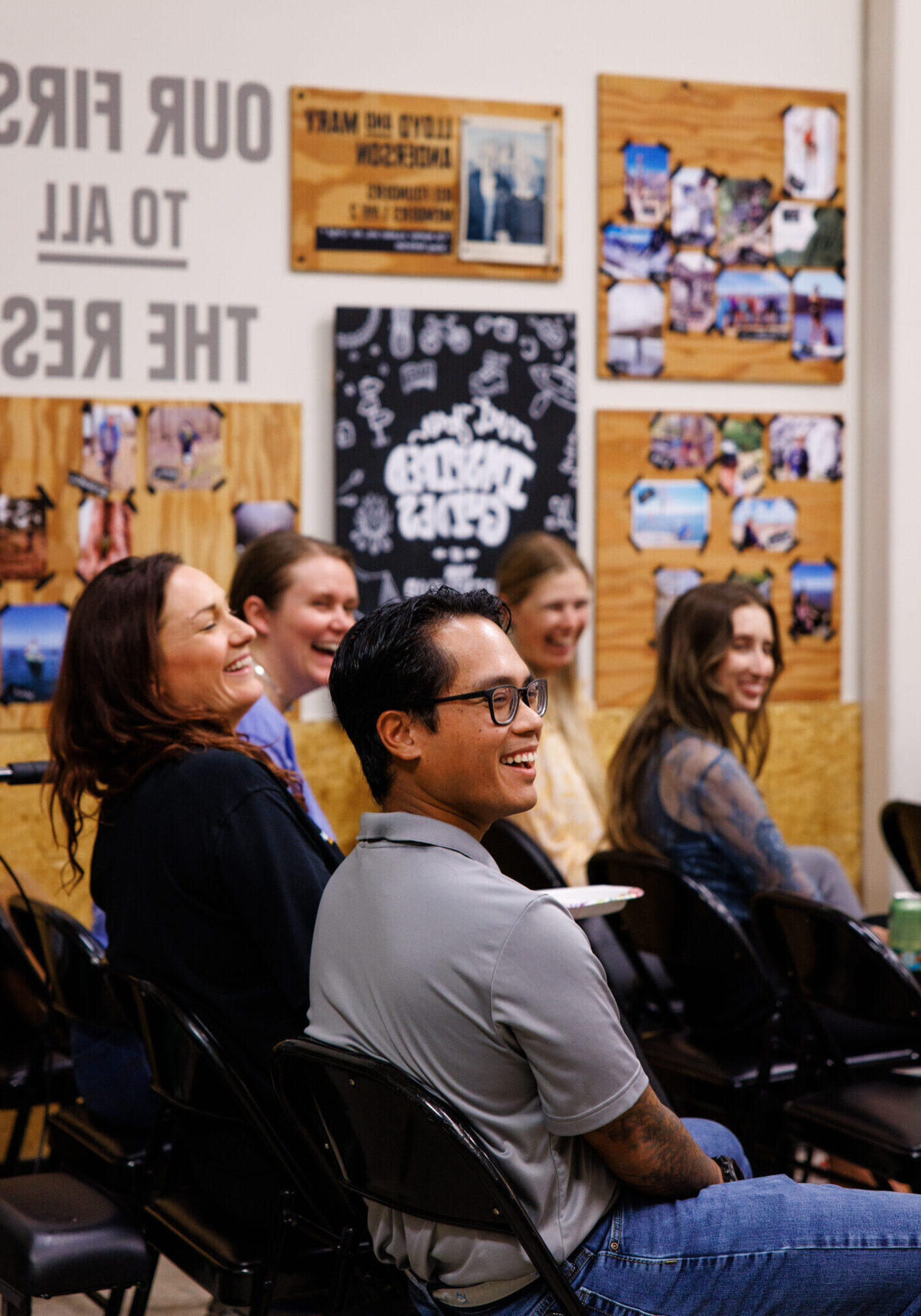 Group of people sitting in black folding chairs set in rows laugh and smile