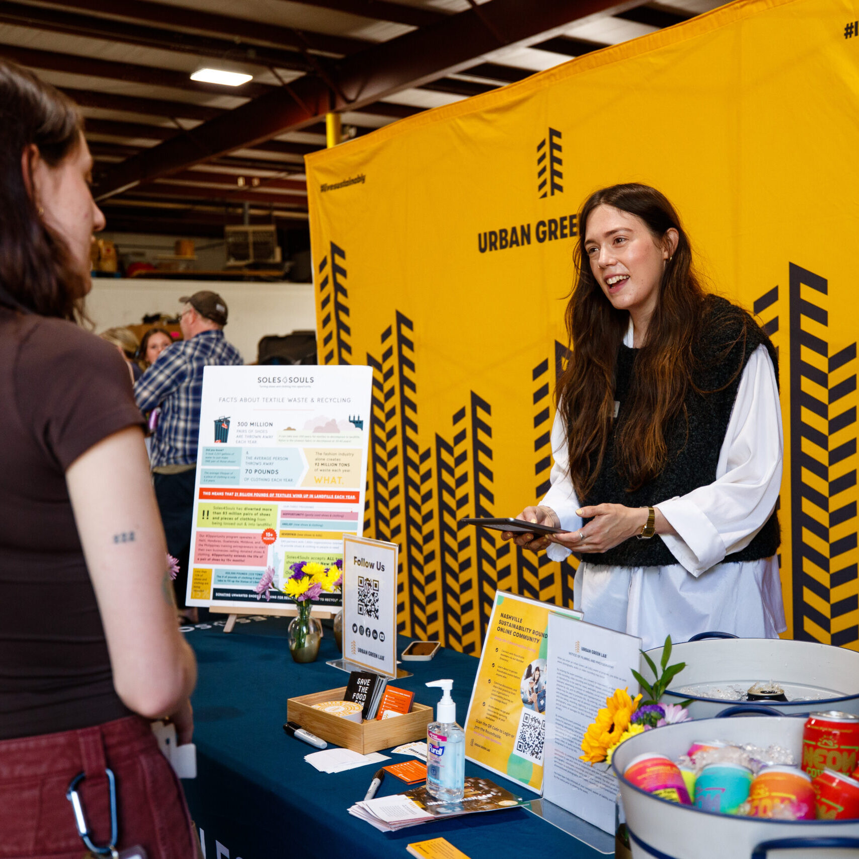 Woman welcomes people to an event with an Urban Green Lab sign behind her