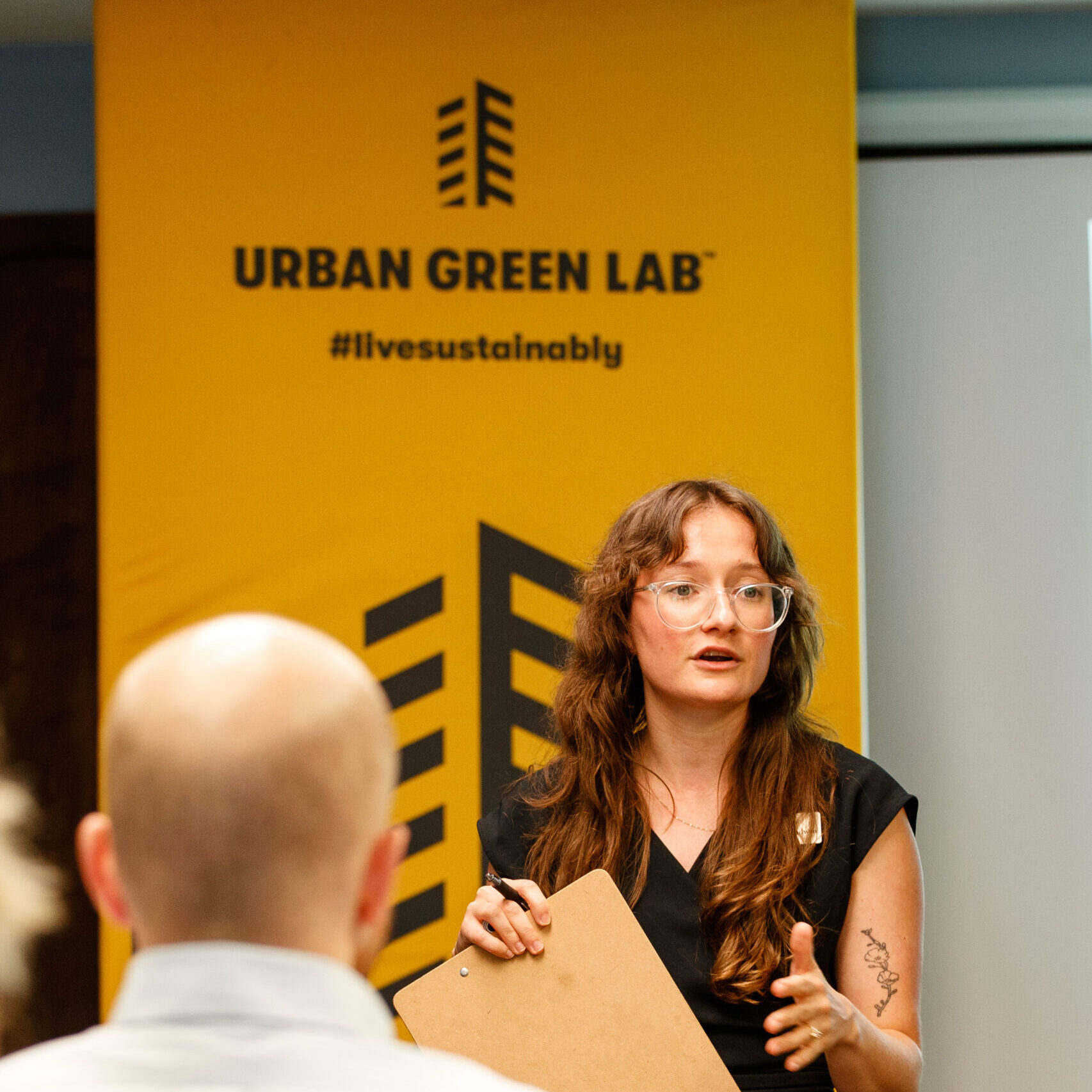 Woman presents to workplaces on sustainability in front of an Urban Green Lab sign