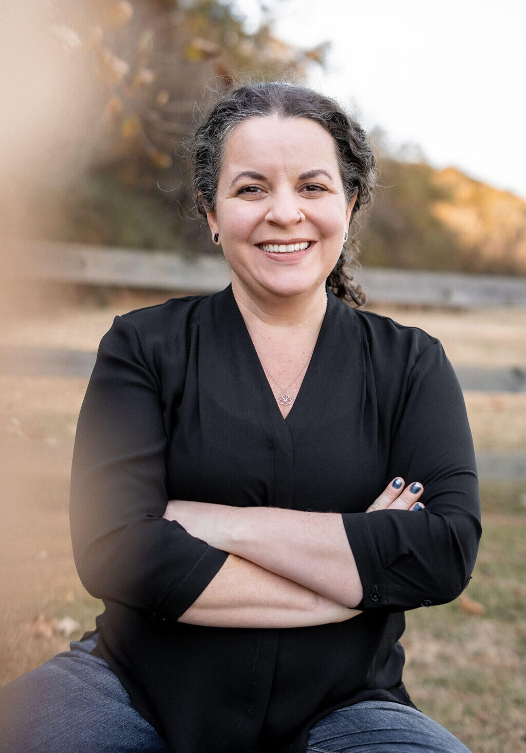 tasha headshot woman in a black blouse smiles with confidently crossed arms in a park with sunset light